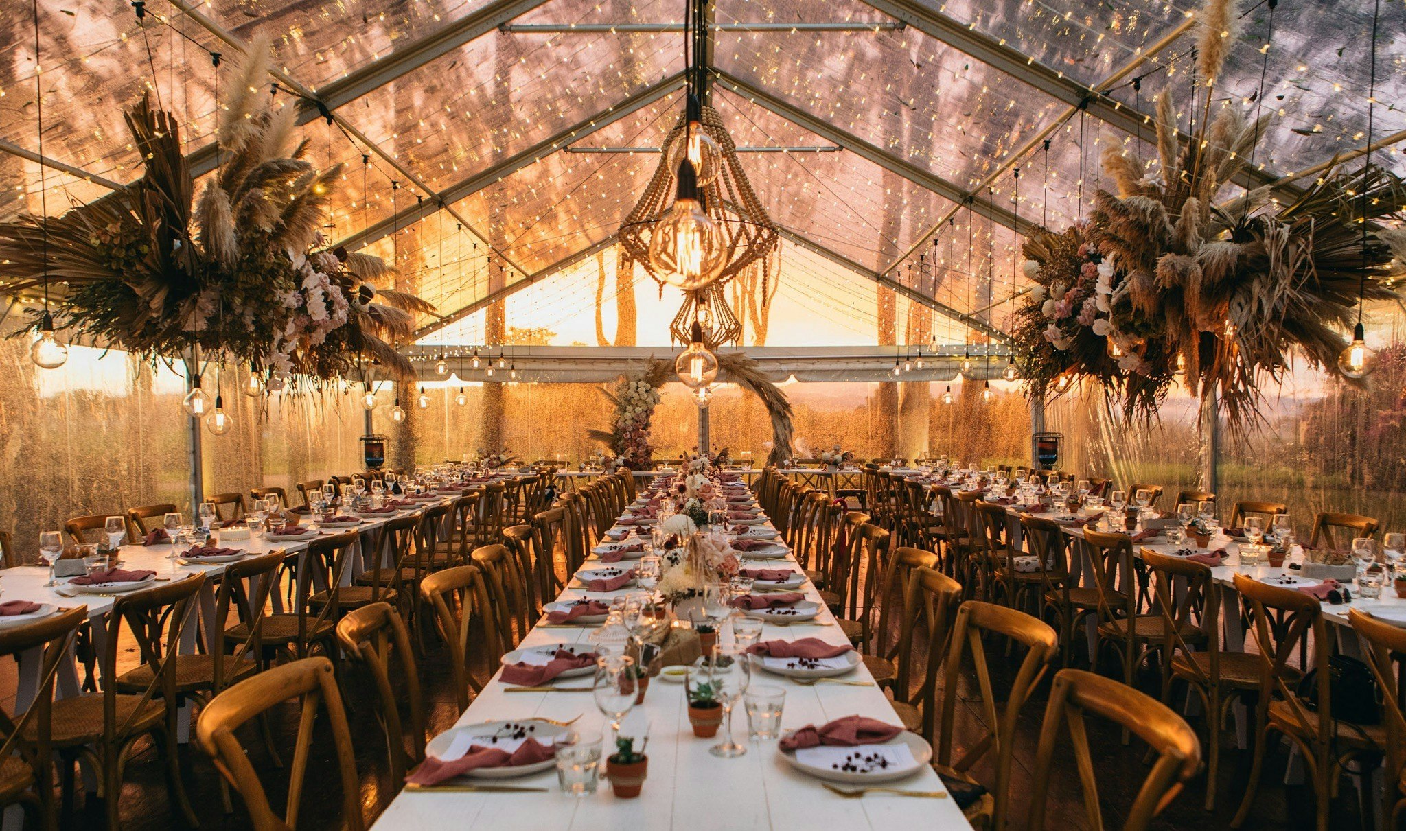 Wedding reception table setting under a marquee at sunset.